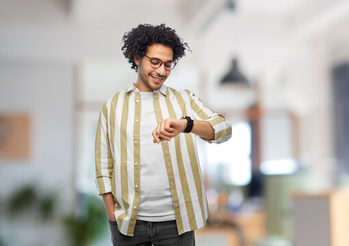 work, technology and people concept - smiling young man in glasses with smart watch over office background