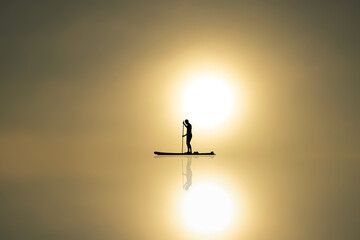 Man stands in a boat and floats on calm water with reflection