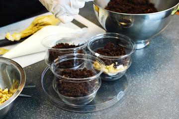 The process of preparing a multi-layered dessert. Confectioner lays out layers of nuts, caramel and biscuit in a plastic mold