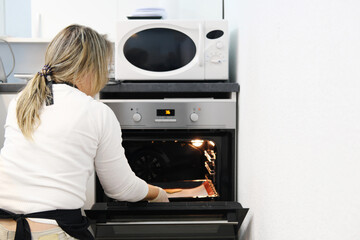 A woman sits with her back to the camera and takes a cookie out of the oven