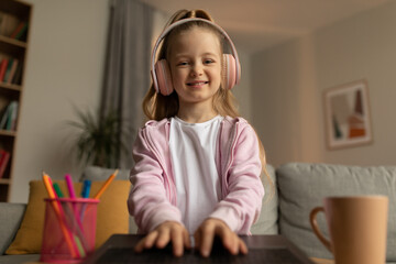 Naklejka premium Happy Kid Girl Typing On Laptop Wearing Headphones At Home