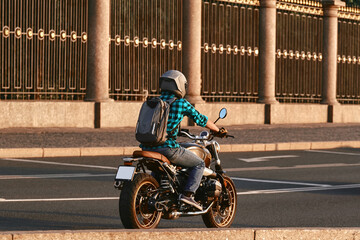 A motorcyclist with a backpack on his back rides a motorcycle along the road along the fence. A man...