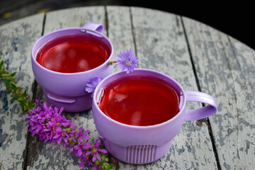 Pink drink in purple cups and wildflowers on a wooden round table