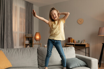 Cheerful Little Girl Dancing Singing Standing On Sofa At Home