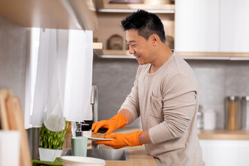 Positive chinese man washing dishes at home