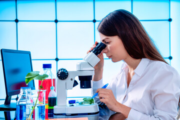 Young woman with microscope in GMO laboratory. Study of green plant of agricultural plants with a microscope