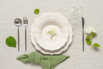 Wedding table setting. Beige plates, a green linen napkin and white hydrangea flowers on a beige linen tablecloth. Top view, flat lay. Selective focus.