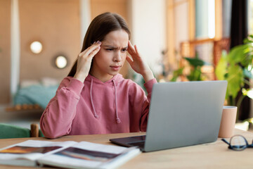 Exhausted schoolgirl suffering from headache, overworking, having too much online homework, looking at laptop