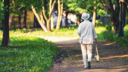 An elderly woman in white walks through a summer park.