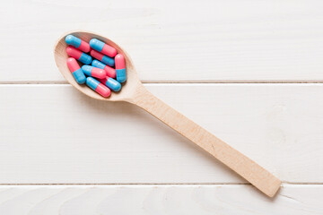 Vitamin capsules in a spoon on a colored background. Pills served as a healthy meal. Red soft gel vitamin supplement capsules on spoon