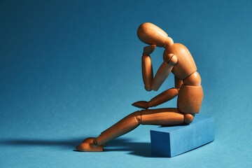 A sad wooden mannequin sits on a chair. Sadness concept