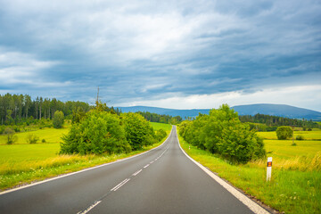 View of road between green tree forest in Czech republic. Car moving on road.