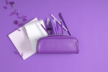 Back to school. Purple pencil case with pencils and notebooks on purple background. Office desk...