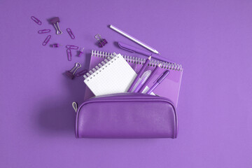 Back to school. Purple pencil case with pencils and notebooks on purple background. Office desk...