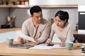 Serious asian family counting monthly expenses, kitchen interior