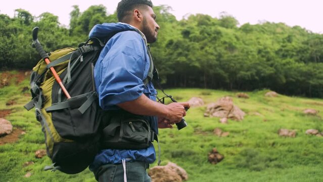 A young male trekker with backpack taking pictures of the verdant mountains.