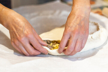 Women's hands sculpt from the dough a large pirok with potatoes and msyaom. Home national cuisine