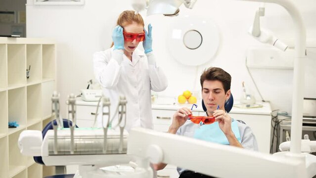 Female dentist giving UV protective glasses to young man during composite filling dental procedure