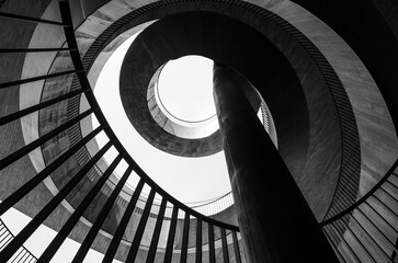 Bottom view of a geometric abstraction in the form of a spirally twisted metal staircase with a railing. Black and white photo