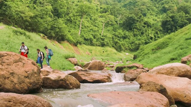 A group of trekkers with backpacks crossing a stream in the midst of beautiful nature.