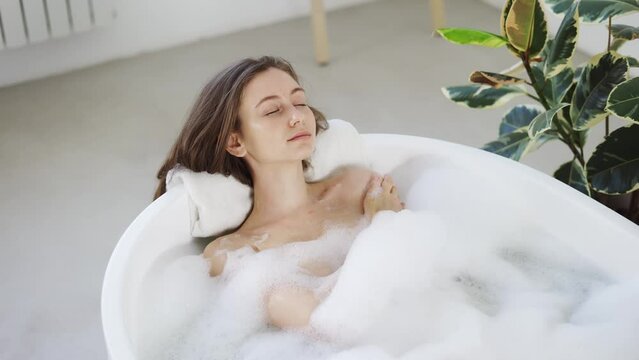 Sexy girl taking bathtub with bubbles and foam in slow motion. Top view of pretty lady enjoying in luxury bathroom