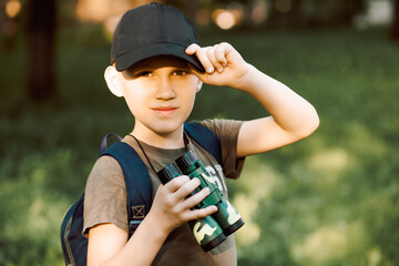 Little boy scout with backpack and binoculars during hiking in forest. Concepts of adventure, journey, scouting and hiking tourism for kids.