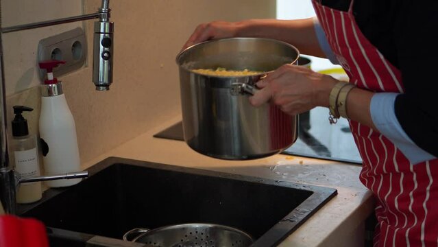 Cooking Bryndzove Halusky - Woman Pouring Boiled Lumps Of Potato Dough Into Strainer On The Kitchen Sink. - crop