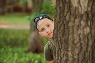 Little boy looking out from behind a tree. Summer activity. Happy childhood.