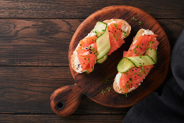 Sandwiches. Salmon toast with cream cheese, cucumber, black sesame and microgreens on old wooden table background. Seafood. Healthy food. Photography in low key. Top view.