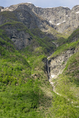 Large waterfall that rises in the mountains surrounded by green trees in Norway.