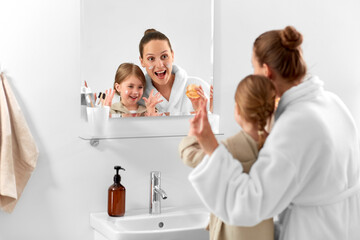 beauty, family and people concept - happy smiling mother and daughter with moisturizer in bathroom