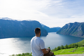 Unrecognizable male tourist photographer with camera in hand, looking out over the stunning Naeroyfjord in Norway.