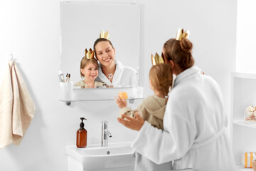 beauty, family and people concept - happy smiling mother and daughter in crowns looking to mirror in bathroom