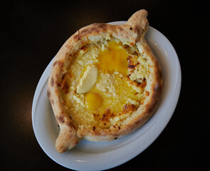 Khachapuri Adjaruli (Georgian Cheese Bread Boat) made with bread, cheese, butter and egg Yolk in a white plate  with black background