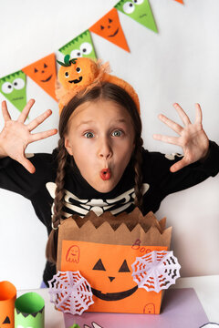 A little girl in a skeleton costume and a headband with a pumpkin makes: boo. Schoolgirl with a bag of sweets