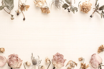 Decorative frame consisting of pink beige roses and other dried flowers on a light wood table...