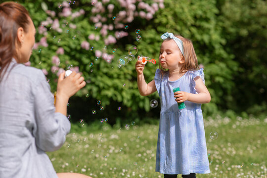childhood, leisure and people concept - little girl with mother blowing soap bubbles at summer park or garden