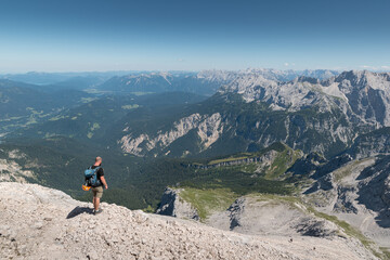 Fototapeta na wymiar Mountaineer at the summit from the Alpspitze in Germany looks down to the valley and to the Karwendel mountains.