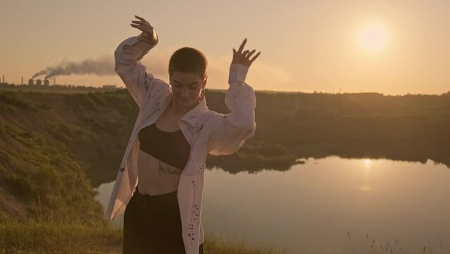 Beautiful woman dancing at sunset. Portrait of carefree dreaming female outdoors. Lake. Concept of freedom in 4K, UHD