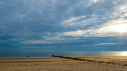 Sand  beach and sand dunes along a sea under a dusk cloudy sky at a bright sunset in summer, Walcheren, Zeeland, the Netherlands, July, 2022