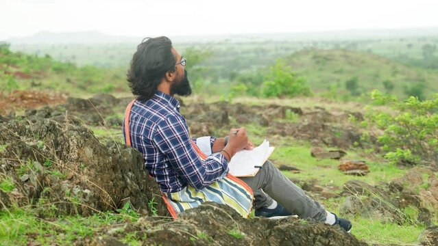 side shot of creative author seriously writing novel while sitting on top of hill by thinking - conept of wisdom, intelligence and contemplation