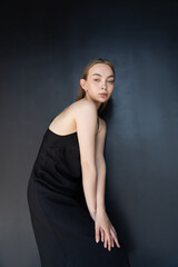 trendy woman in strap dress looking at camera while posing on black background.