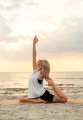 Fototapeta na wymiar fitness, sport, and healthy lifestyle concept - woman doing yoga mermaid pose on beach over sunset