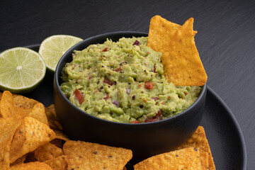 Guacamole dip with tortilla chips or nachos and lime on a black background