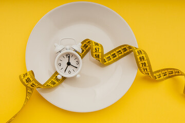 White alarm clock on white plate with measuring tape on a yellow background. Concept of...