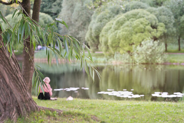 Obraz na płótnie Canvas young woman sitting by the lake in a forest and relaxing. enjoying nature, peaceful place for rest and meditation. staying alone, local travelling.
