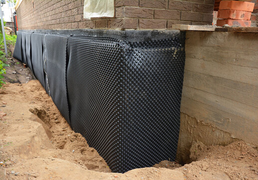 House foundation waterproofing. Installation of a dimpled waterproofing membrane on the exterior brick house basement wall.