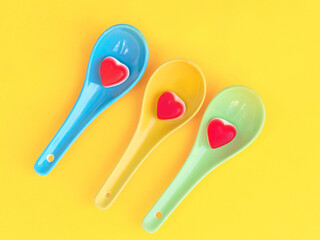 Colourful spoons with Candy Heart Sweets with a vibrant yellow background. 