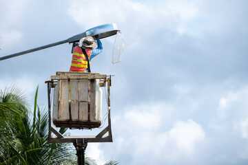 Male worker sitting on a chairlift to light a street lamp, work safety.