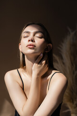 Fototapeta premium seductive woman with closed eyes and natural makeup touching neck on dark background.